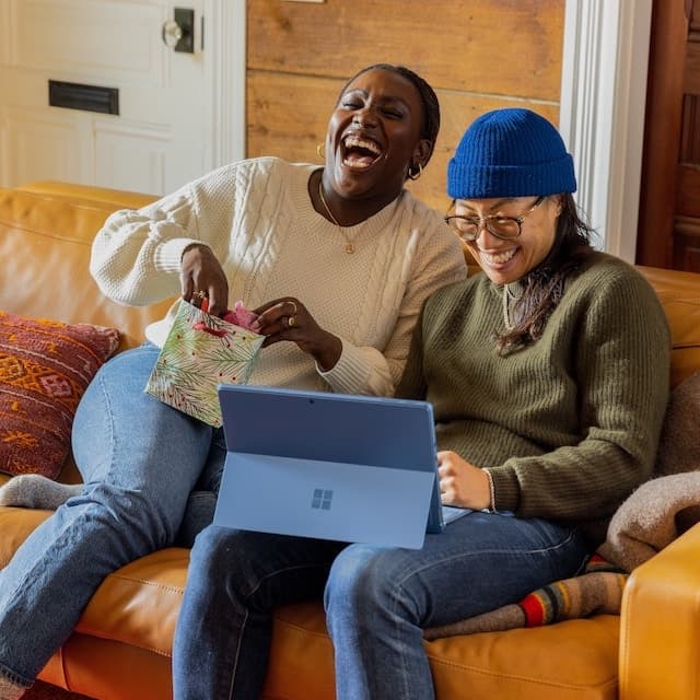 A couple sits on the couch chuckling.