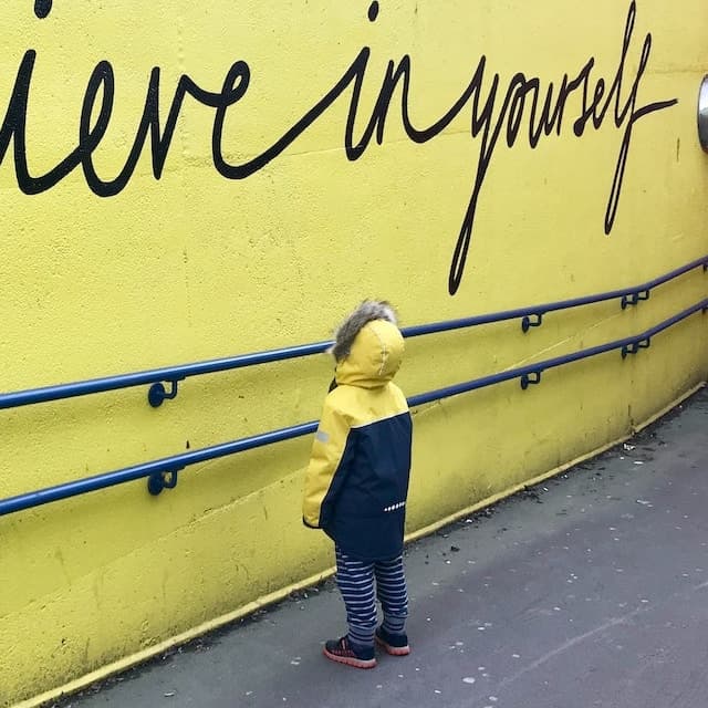 Small child looks at a wall with an inspirational quote.